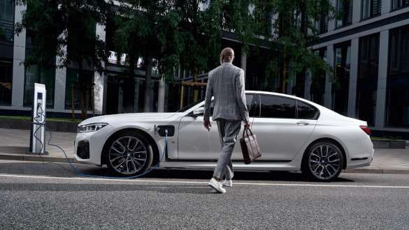 BMW 745e limuzina plug-in hybrid G11 G12 Mineral White metalik pogled s boka ispred stanice za punjenj BMW 745e limuzina plug-in hybrid G11 G12 Mineral White metalik pogled s boka ispred stanice za punjenje sa modelom