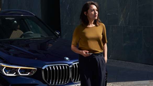 BMW Roadside Assistance. BMW Roadside Assistance žena sa pametnim telefonom ispred BMW-a