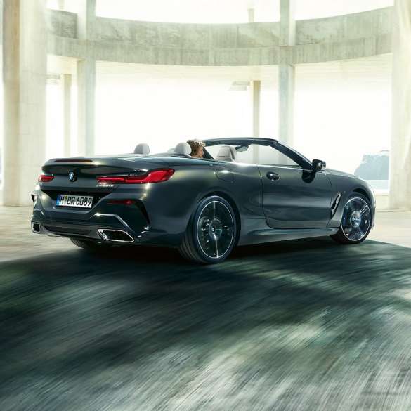 BMW M850i xDrive Cabrio, tročetvrtinski prikaz stražnjeg kraja. BMW M850i xDrive Cabrio u Dravit Grey metalik boji, sa spuštenim mekim krovom, tročetvrtinski prikaz stražnjeg kraja, u vožnji kroz betonsku zgradu.