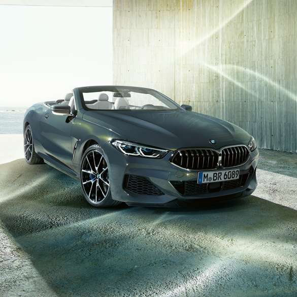 BMW M850i xDrive Cabrio, tročetvrtinski prikaz prednjeg kraja. BMW M850i xDrive Cabrio u Dravit Grey metalik boji, sa spuštenim mekim krovom, tročetvrtinski prikaz prednjeg kraja, ispred obale.