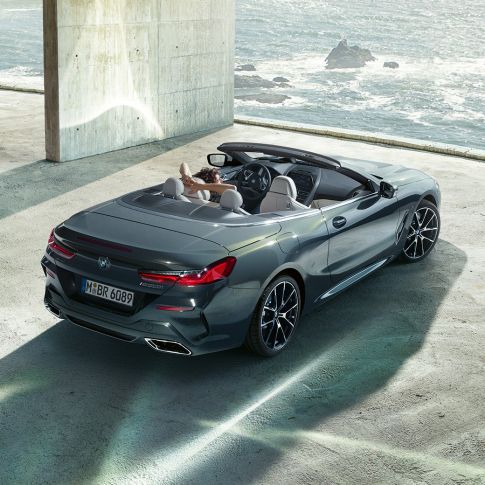 BMW M850i xDrive Cabrio, prikaz iz ptičje perspektive. BMW M850i xDrive Cabrio u Dravit Grey metalik boji, sa spuštenim mekim krovom, prikaz iz ptičje perspektive, parkiran u betonskoj zgradi ispred oceana.