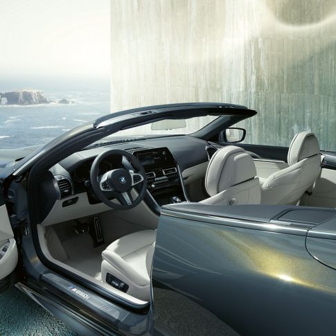 BMW M850i xDrive Cabrio, unutrašnjost. BMW M850i xDrive Cabrio u Dravit Grey metalik boji, sa spuštenim mekim krovom, unutrašnjost s M kožnim upravljačem i BMW Individual unutrašnjošću od 'Merino' kože u Ivory White boji.
