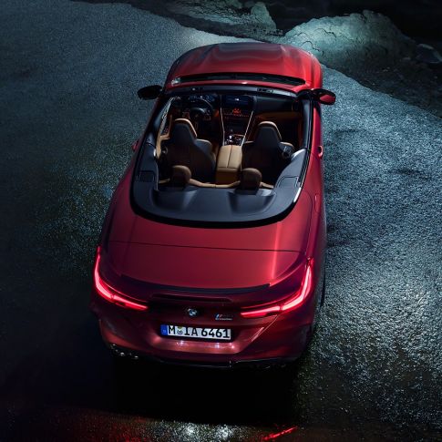 BMW M8 Competition Cabrio, prikaz iz ptičje perspektive. BMW M8 Competition Cabrio u Motegi Red metalik boji sa spuštenim mekim krovom, prikaz iz ptičje perspektive, noću na asfaltu.