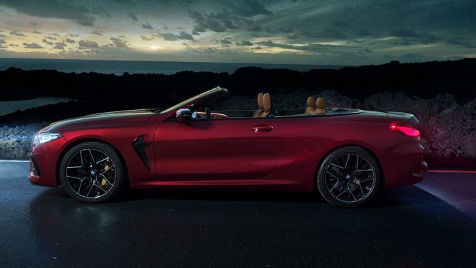 BMW M8 Competition Cabrio, bočni prikaz. BMW M8 Competition Cabrio u Motegi Red metalik boji sa spuštenim mekim krovom, bočni prikaz, noću pod zvjezdanim nebom.