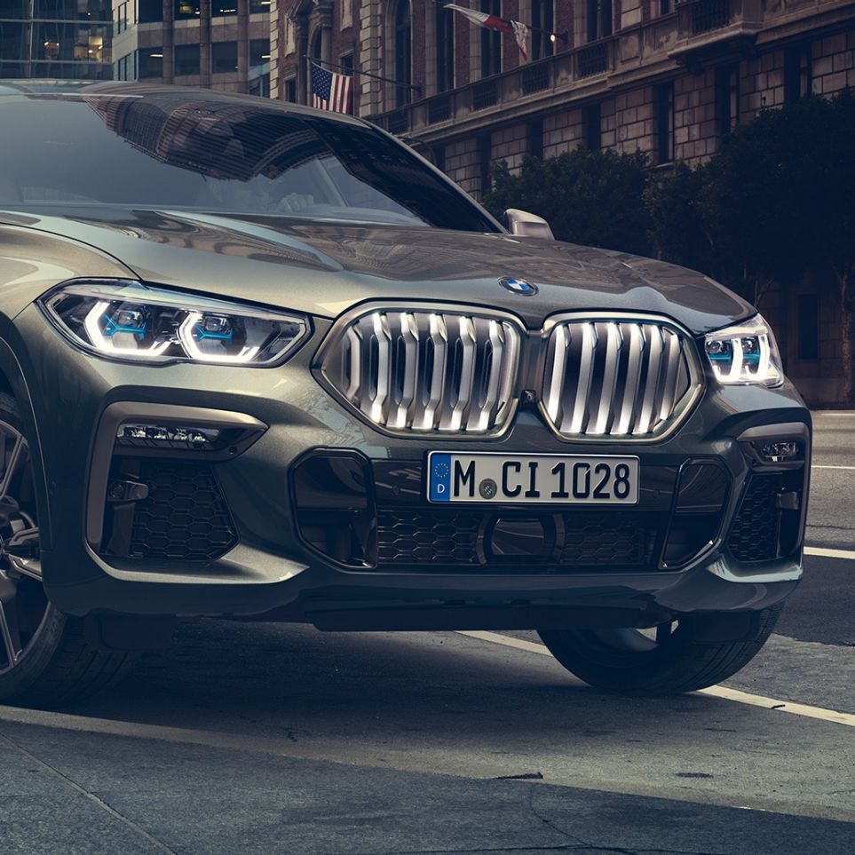 Stacionarni BMW X6 M50i BMW X6 M50i u tročetvrtinskoj perspektivi prednjeg kraja ispred urbane pozadine