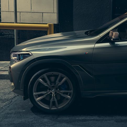 BMW X6 M50i u bočnoj perspektivi Čovjek naslonjen na BMW X6 M50i u bočnoj perspektivi ispred urbanog okruženja