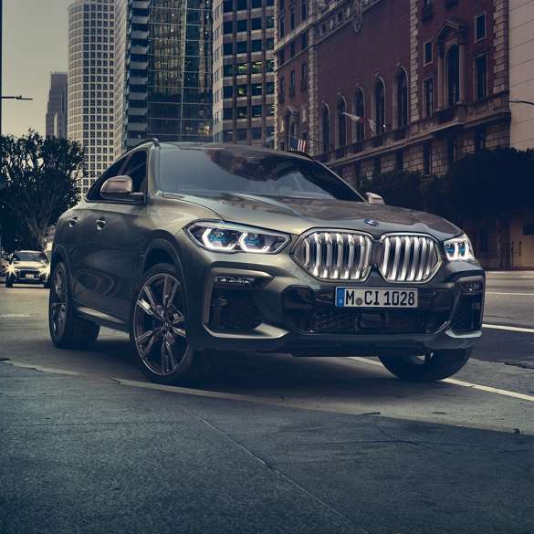 BMW X6 prilagodljiv M ovjes Professional BMW X6 u tročetvrtinskom prikazu prednjeg kraja ispred urbanog okruženja.