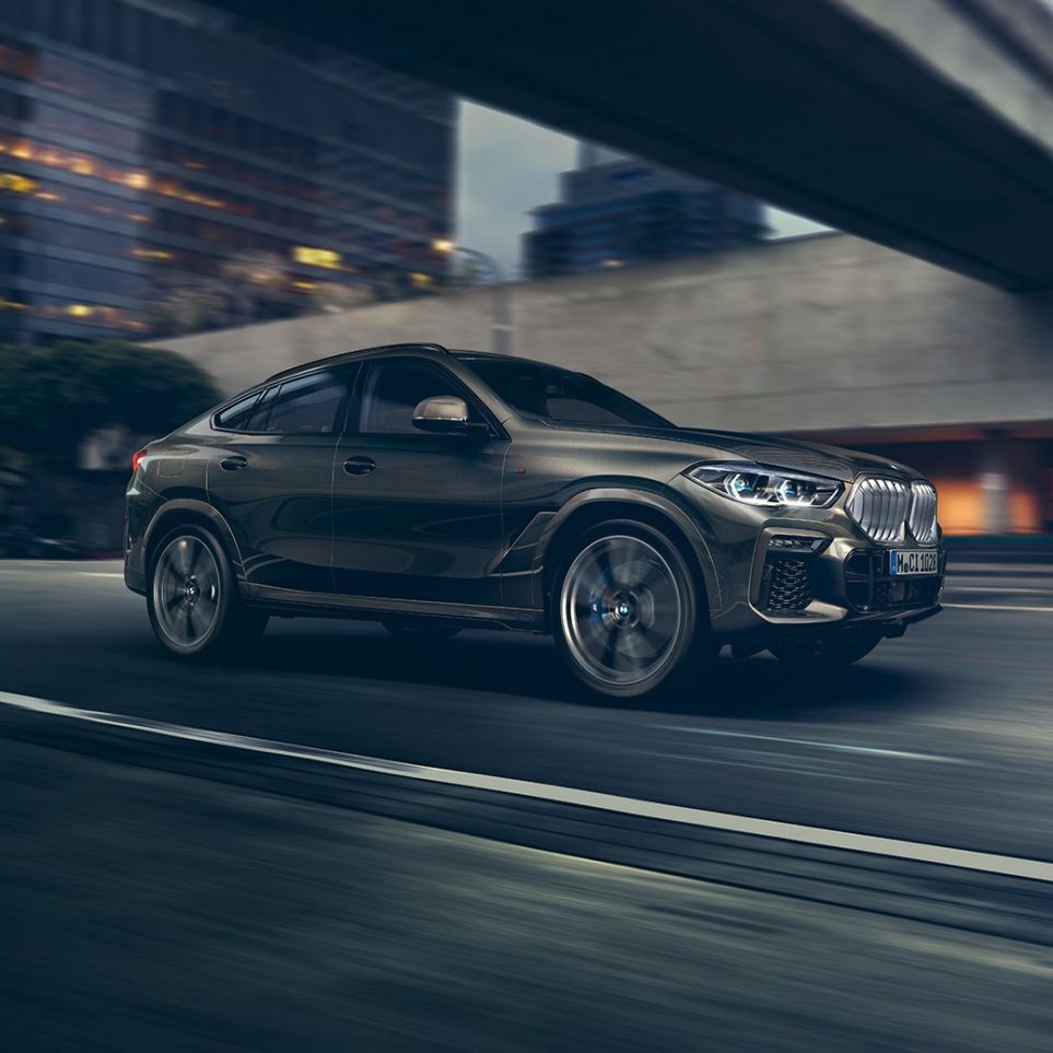 BMW X6 u vožnji. Tročetvrtinska perspektiva prednjeg kraja BMW-a X6 u vožnji ispred urbanog okruženja.