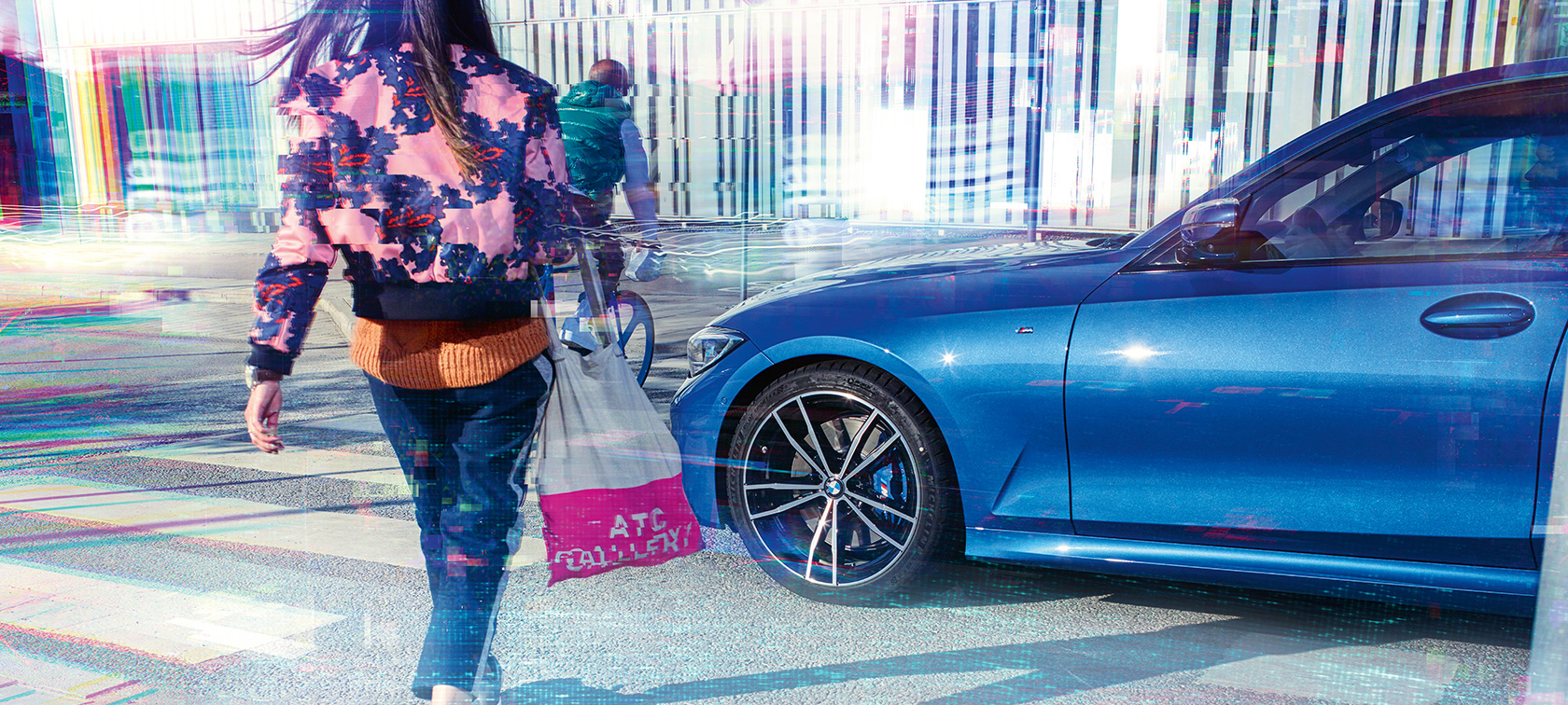 BMW serije 3 Limuzina, tročetvrtinski bočni prikaz. Tročetvrtinski bočni prikaz BMW-a serije 3 limuzina na asfaltu ispred urbane pozadine s putnicima.