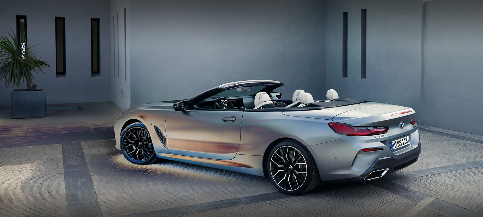 Muškarac se naginje nad BMW serije 8 Cabrio G14 LCI Facelift 2022 BMW Individual Frozen Pure Grey metalik u pogledu s boka u mirovanju ispred zgrade sa muškim modelom