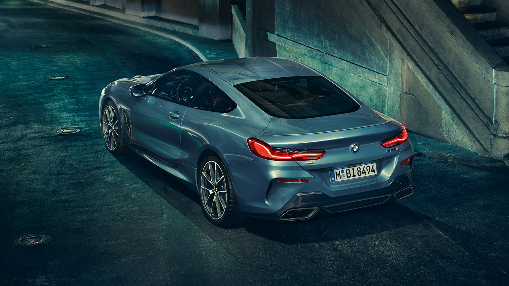 BMW serije 8 Coupé, tročetvrtinski stražnji prikaz Tročetvrtinski stražnji prikaz BMW-a serije 8 Coupé noću ispred urbanog okruženja.