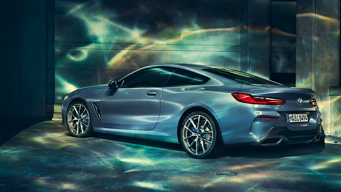 BMW serije 8 Coupé, tročetvrtinski prikaz stražnjeg kraja. Tročetvrtinski prikaz stražnjeg kraja BMW-a serije 8 Coupé noću ispred urbanog okruženja.