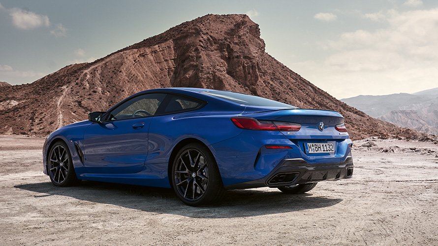 Tročetvrtinski pogled straga BMW serije 8 Coupé M sport paketom G15 LCI Facelift 2022 BMW serije 8 Coupé M sport paket G15 LCI Facelift 2022 M Portimao Blue metalik tročetvrtinski pogled straga u mirovanju ispred stijena