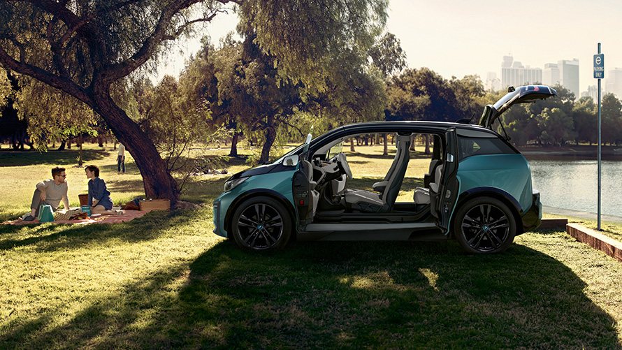 BMW i3 2018 u parku Bočni prikaz BMW-a i3 I01 2018 Jucaro bež boje s Frozen Grey metalik detaljima s otvorenim vratima u parku