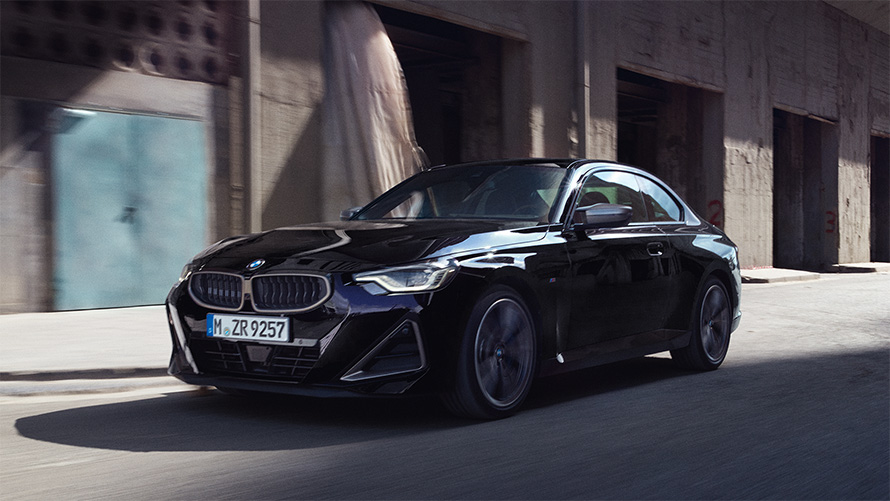 BMW M240i xDrive Coupé G42 2021 tročetvrtinski pogled s boka u vožnji BMW M240i xDrive Coupé G42 2021 Black Sapphire metalik tročetvrtinski pogled s boka u vožnji ispred svjetionika