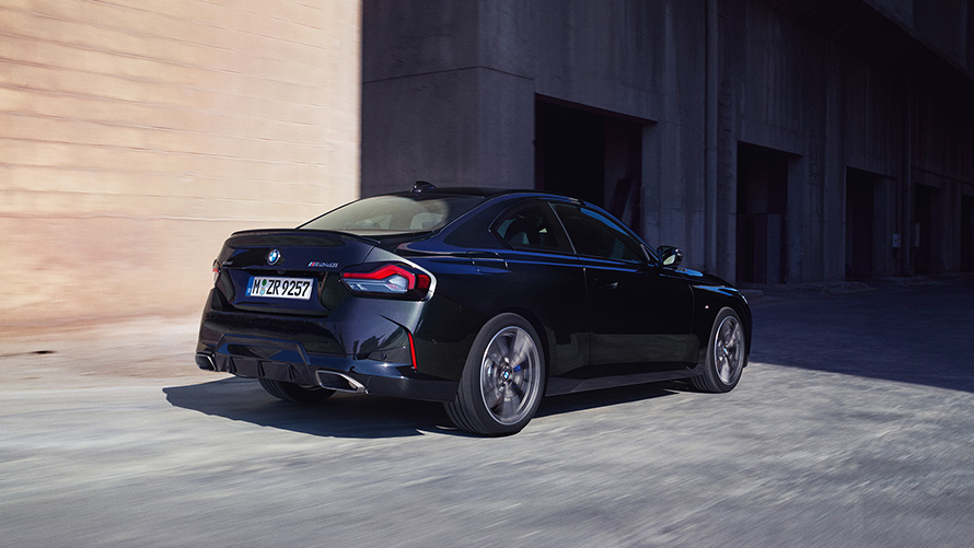 BMW M240i xDrive Coupé G42 2021 tročetvrtinski pogled straga u mirovanju BMW M240i xDrive Coupé G42 2021 Black Sapphire metalik tročetvrtinski pogled straga u mirovanju ispred svjetionika