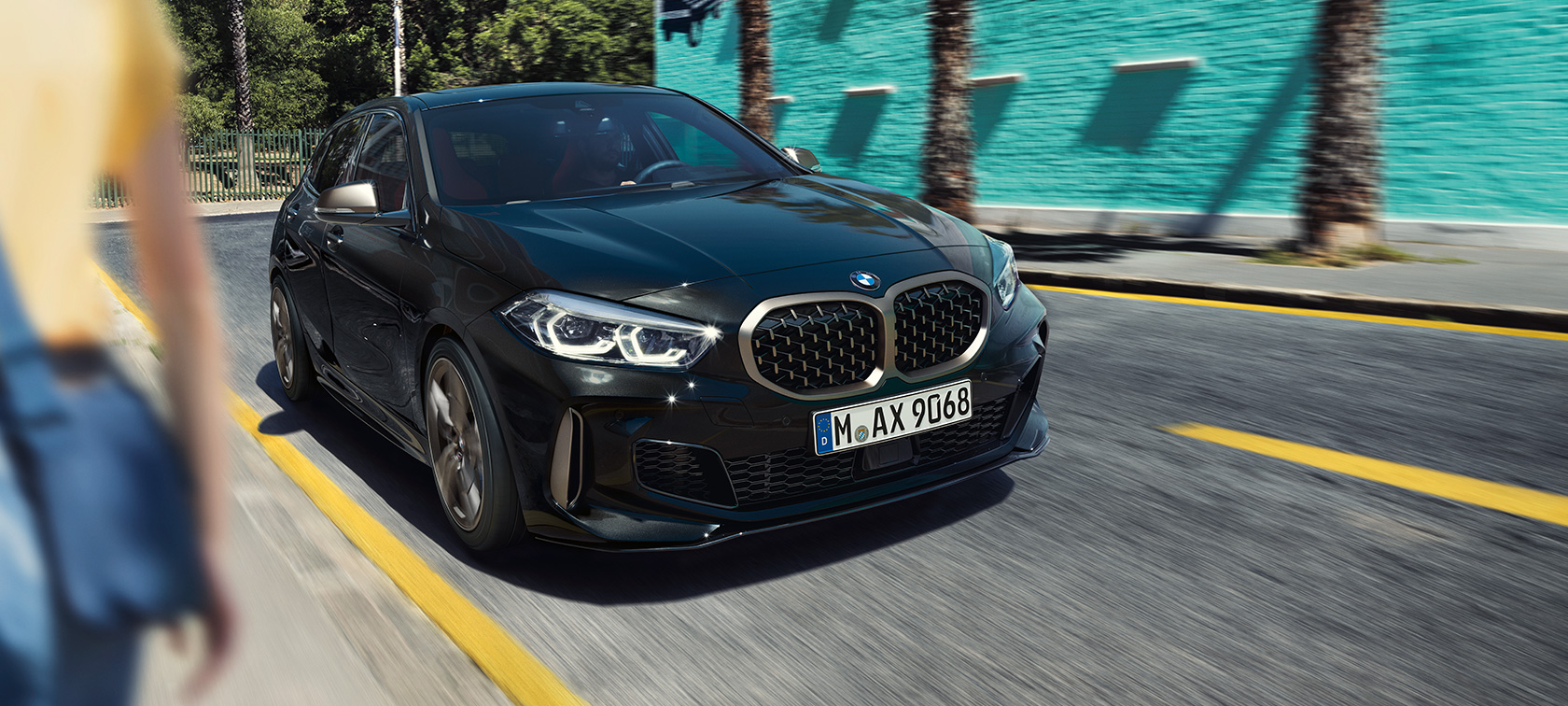 BMW M135i xDrive, tročetvrtinski prikaz prednjeg kraja. BMW M135i xDrive u Black Sapphire metalik boji, tročetvrtinski prikaz prednjeg kraja prilikom vožnje.
