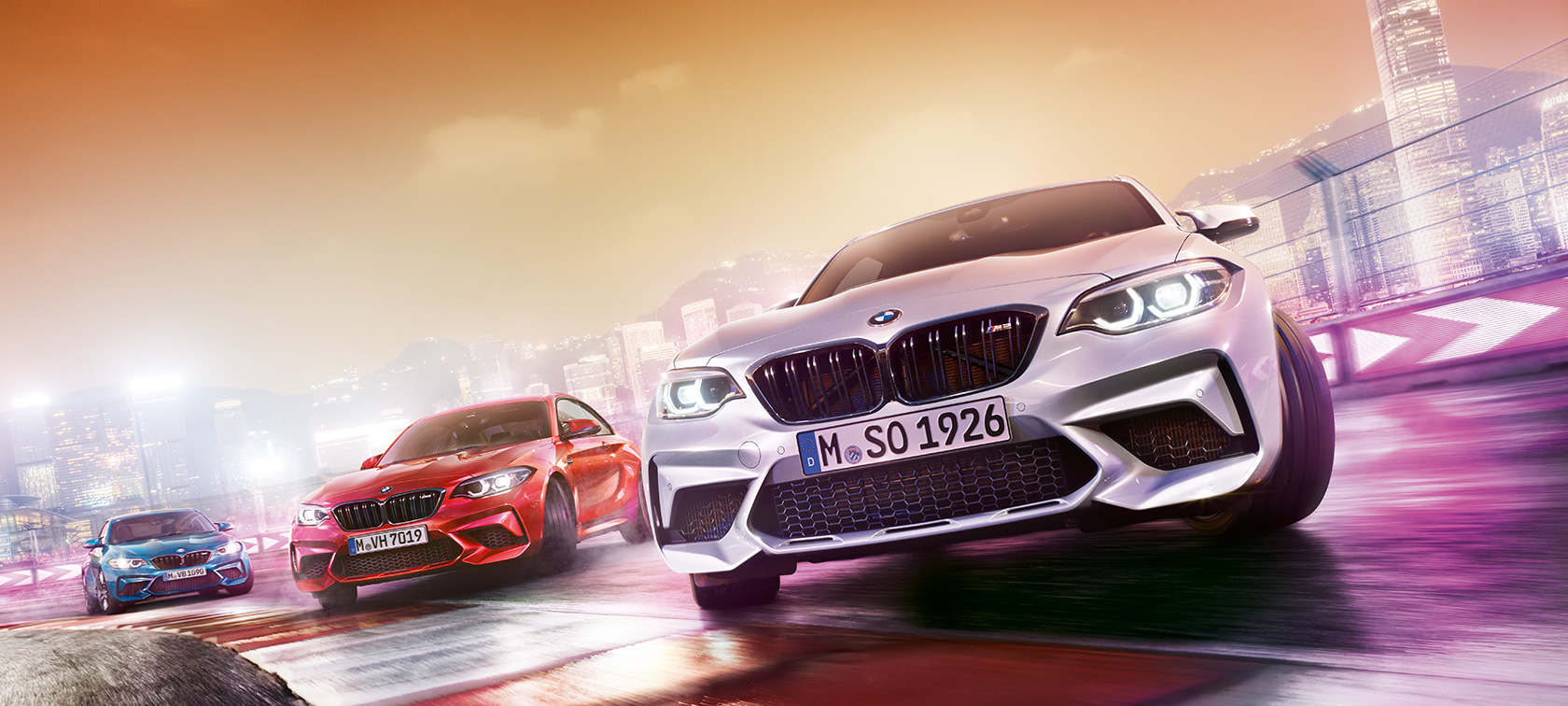 BMW M2 Competition u akciji Tri modela BMW M2 Competition na trkaćoj stazi ispred noćnog pejzaža grada.