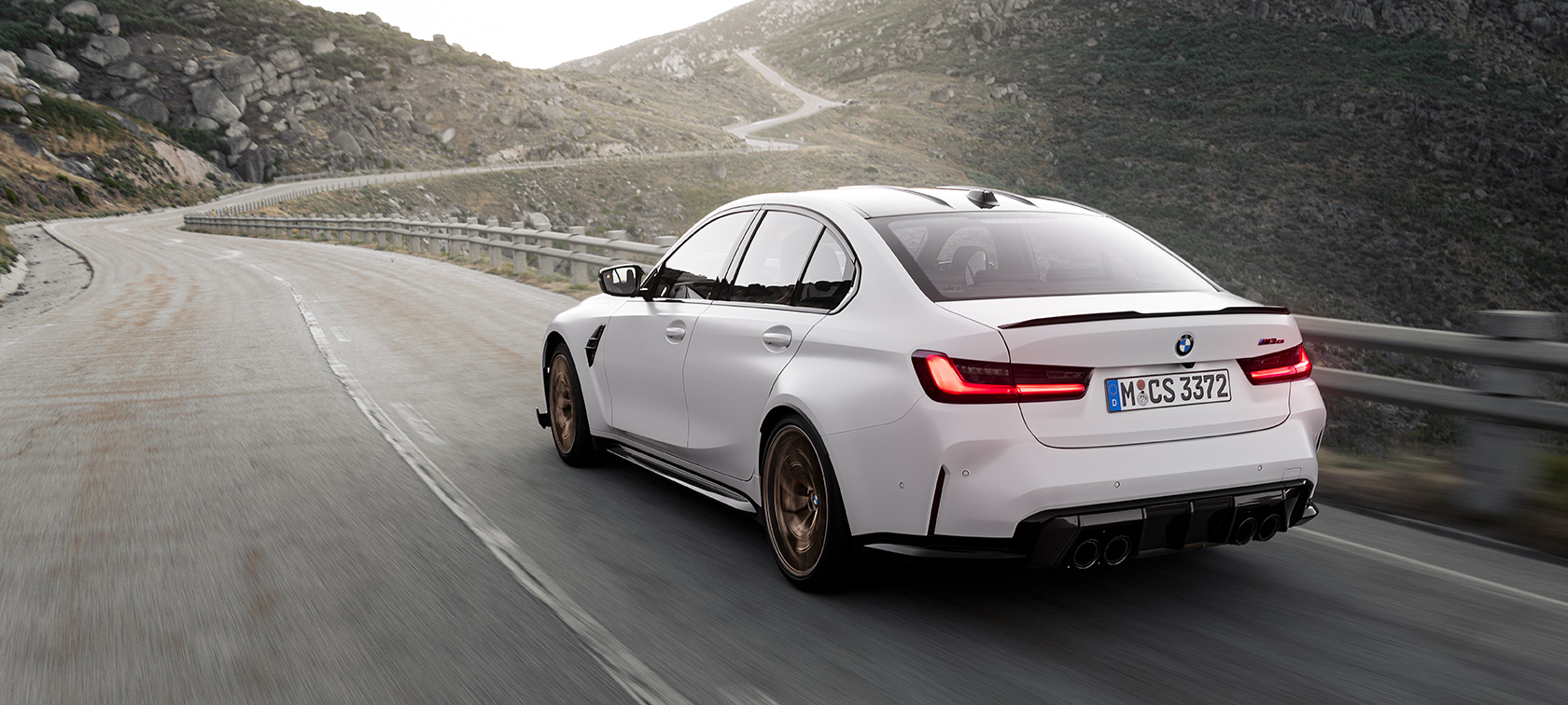 BMW M3 CS G80 tročetvrtinski pogled straga u vožnji BMW M3 CS G80 tročetvrtinski pogled straga u vožnji cestom u planinama