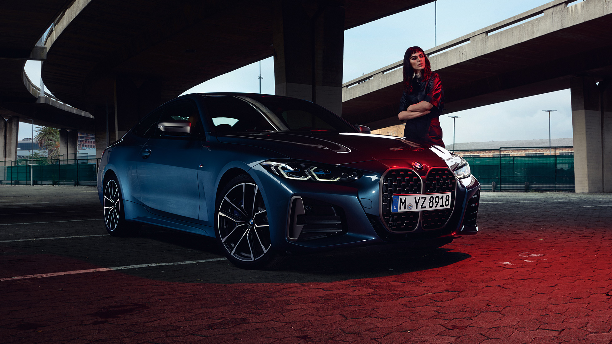 Model stoji pokraj BMW M440i xDrive Coupé G22 2020 tročetvrtinski pogled s boka BMW M440i xDrive Coupé Arctic Race Blue metalik G22 2020 tročetvrtinski pogled s boka sa modelom