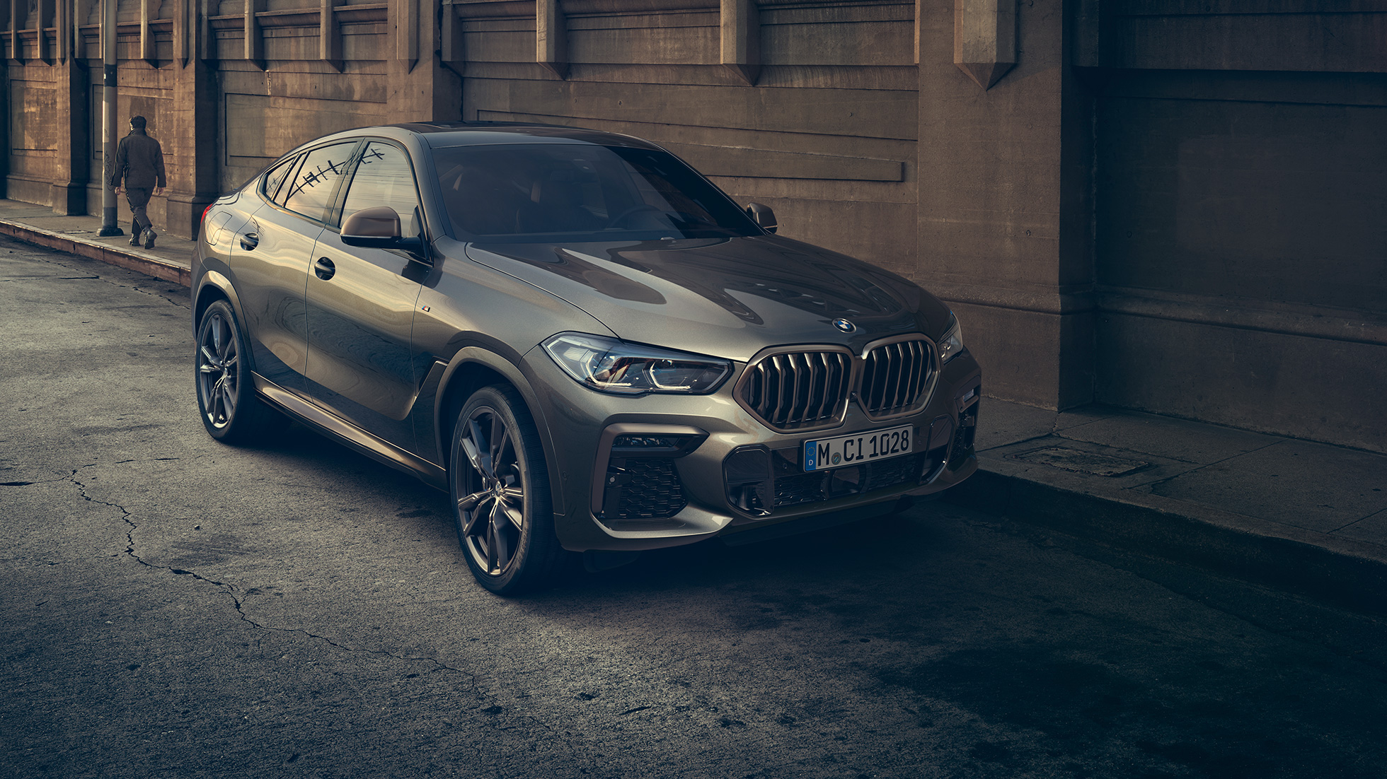 BMW X6 M50i u stacionarnom položaju. BMW X6 M50i u tro-četvrtinskom prikazu prednjeg kraja stoji ispred urbanog okruženja.