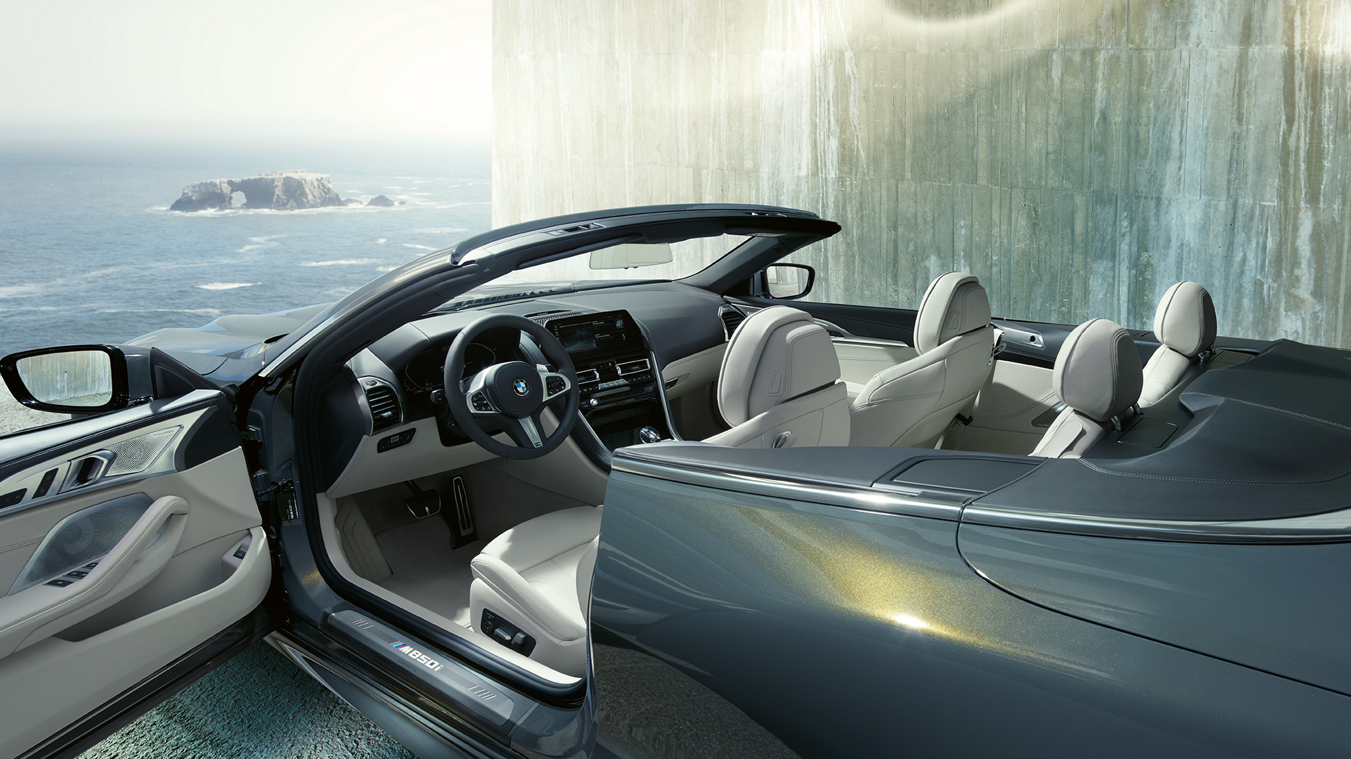 BMW M850i xDrive Cabrio, unutrašnjost. BMW M850i xDrive Cabrio u Dravit Grey metalik boji, sa spuštenim mekim krovom, unutrašnjost s M kožnim upravljačem i BMW Individual unutrašnjošću od 'Merino' kože u Ivory White boji.