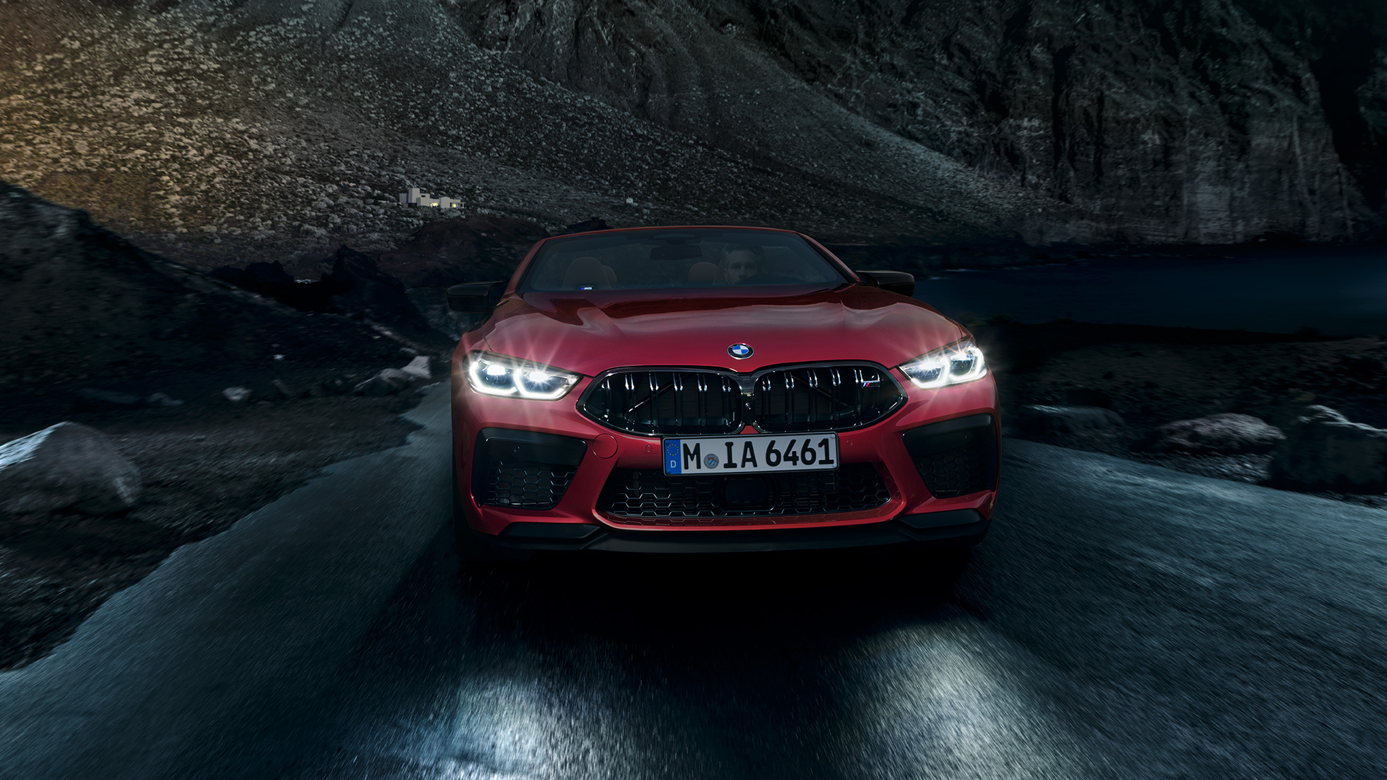 BMW M8 Competition Cabrio, prikaz prednjeg kraja. BMW M8 Competition Cabrio u Motegi Red metalik boji sa sjajnim prednjim svjetlima, prikaz prednjeg kraja, u vožnji noću.