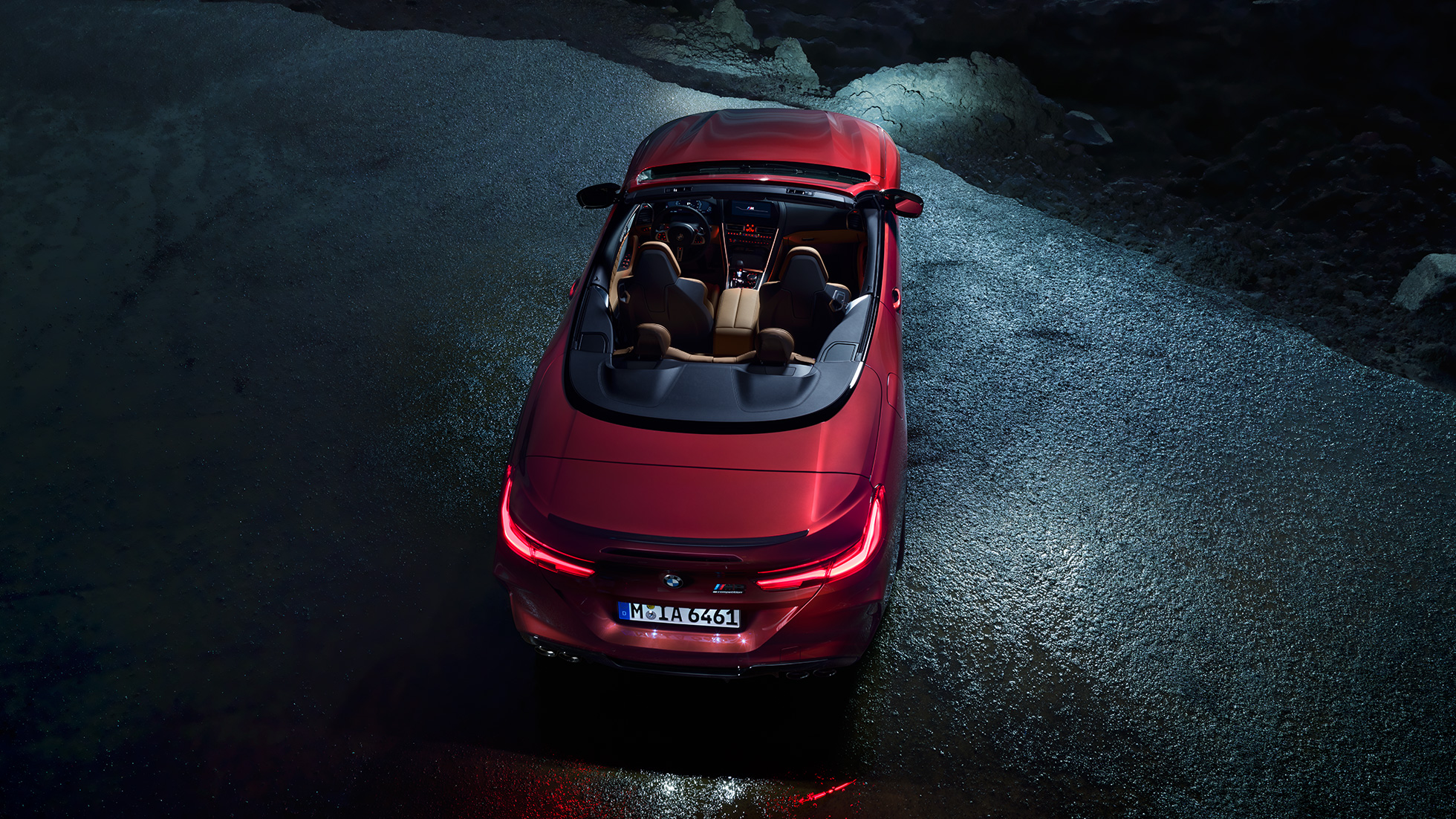 BMW M8 Competition Cabrio, prikaz iz ptičje perspektive. BMW M8 Competition Cabrio u Motegi Red metalik boji sa spuštenim mekim krovom, prikaz iz ptičje perspektive, noću na asfaltu.