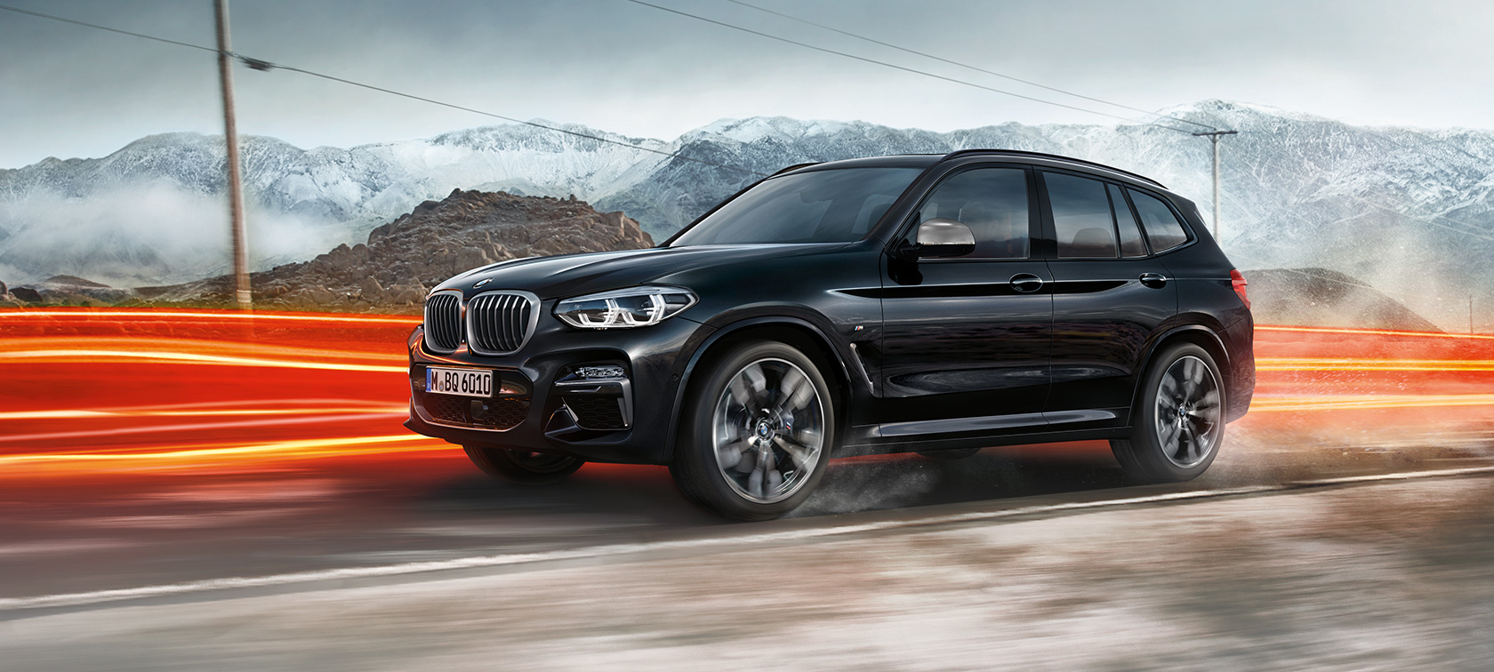 BMW X3 M40i i BMW X3 M40d, bočni prikaz. BMW X3 M40i i BMW X3 M40d u Black Sapphire metalik boji, u vožnji, vanjština, bočni prikaz ispred planinske pozadine sa svijetlosnim trakama.