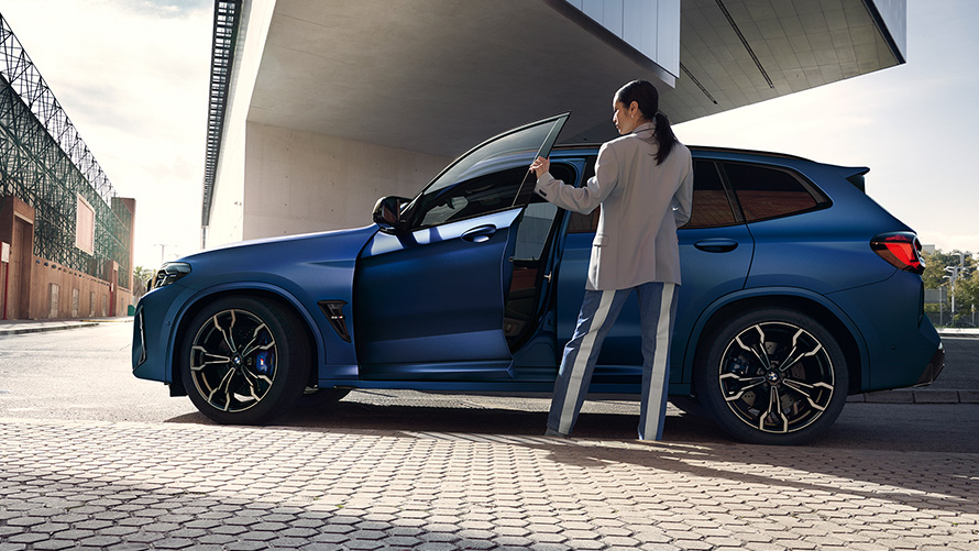 BMW X3 M Competition F97 LCI 2021 pogled s boka sa otvorenim vratima i ženskim modelom BMW X3 M Competition F97 LCI Facelift 2021 Frozen Marina Bay Blue metalik pogled s boka sa otvorenim vratima i ženskim modelom