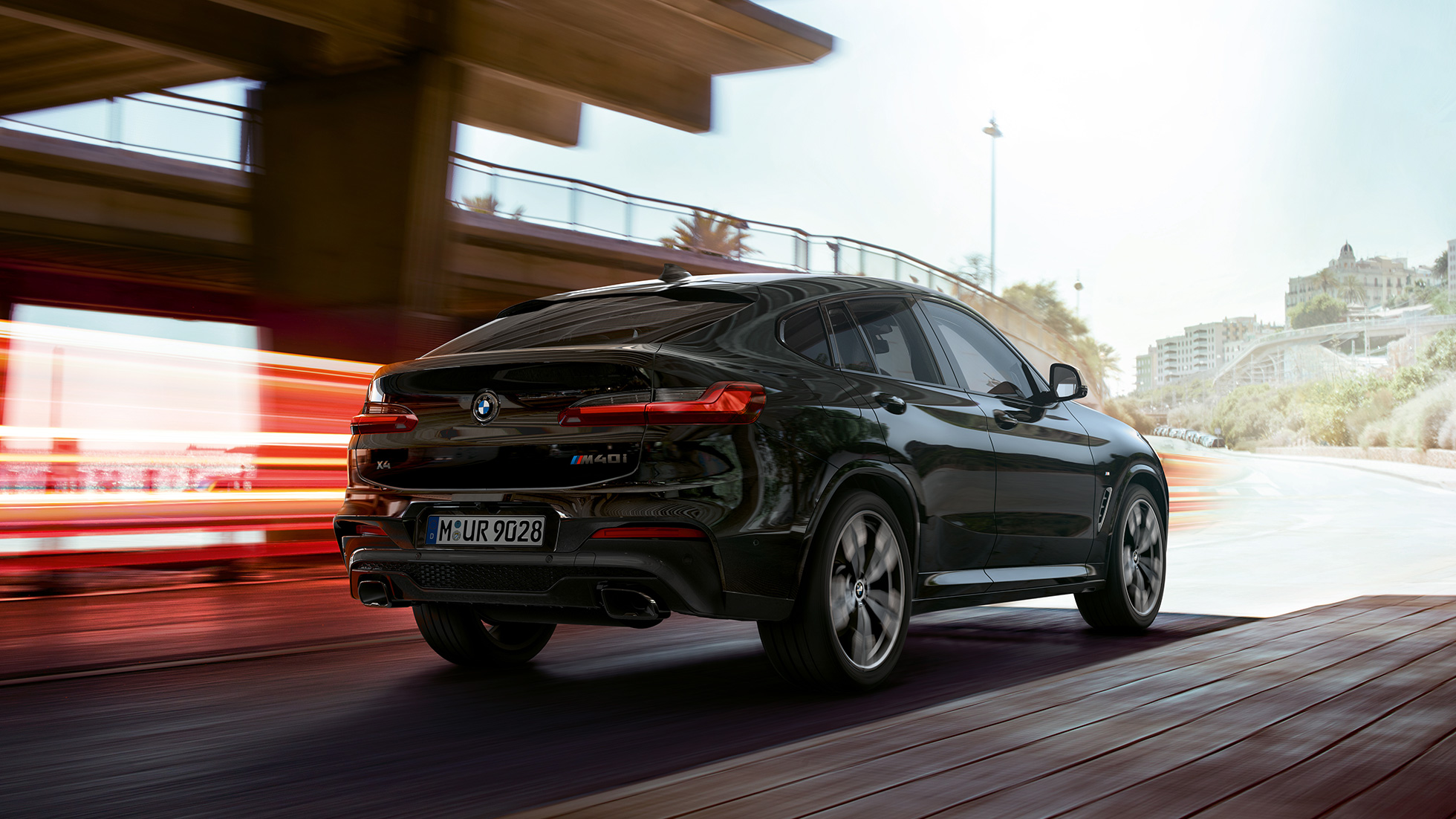 BMW X4 M40i, tročetvrtinski prednji prikaz. BMW X4 M40i u Black Sapphire metalik boji, u vožnji, vanjština, tročetvrtinski prednji prikaz sa svijetlosnim trakama.