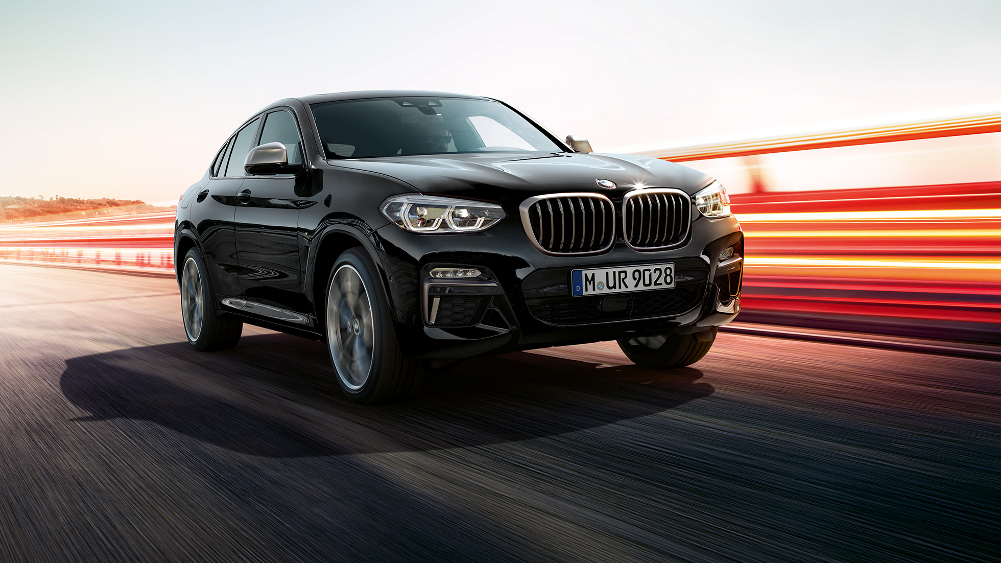 BMW X4 M40i i BMW X4 M40d, tročetvrtinski prednji prikaz. BMW X4 M40i i BMW X4 M40d u Black Sapphire metalik boji, vanjština, tročetvrtinski prednji prikaz, lijeva strana a svjetlosnim trakama.