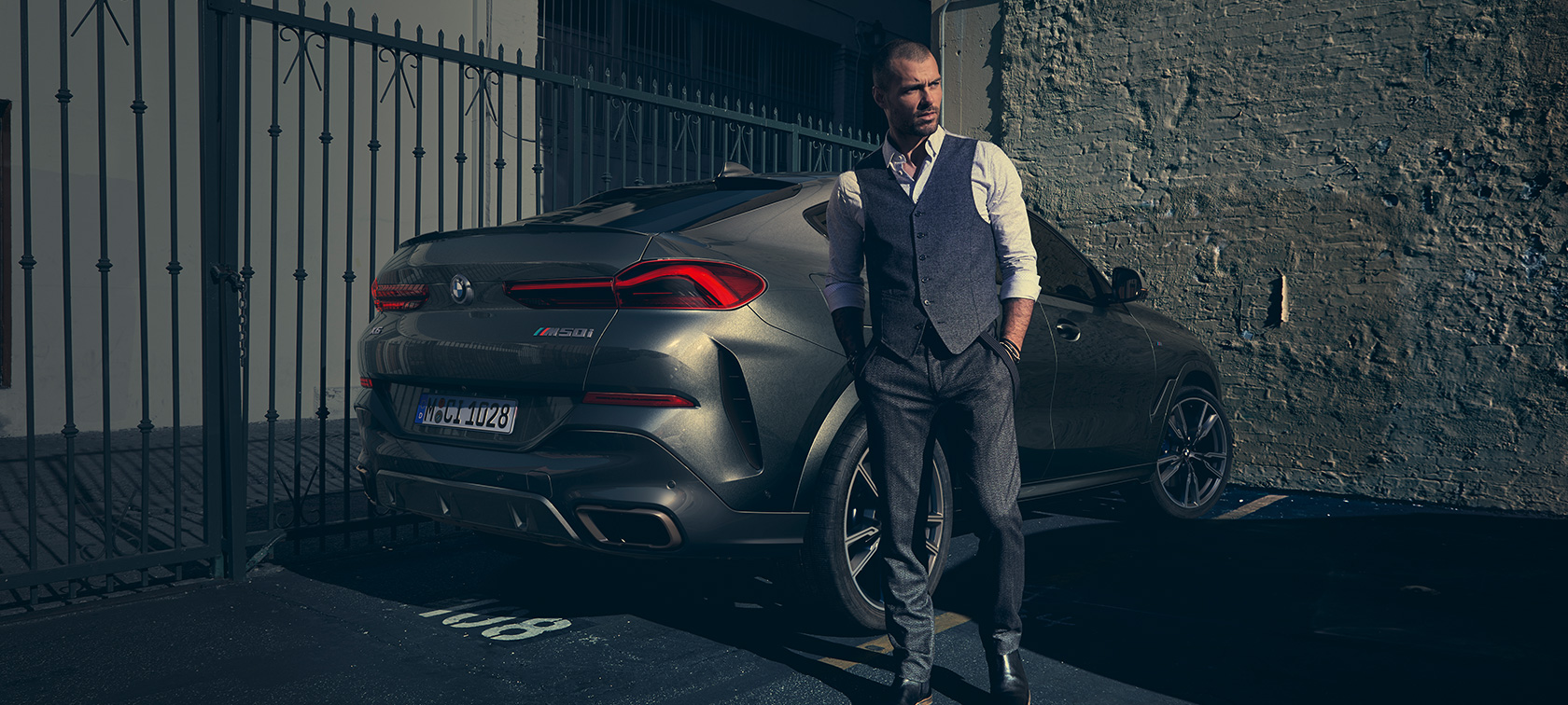 BMW X6 M50i u tročetvrtinskom pogledu straga G06 Muškarac stoji pokraj BMW X6 M50i G06 2018 SUV u tročetvrtinskom pogledu straga