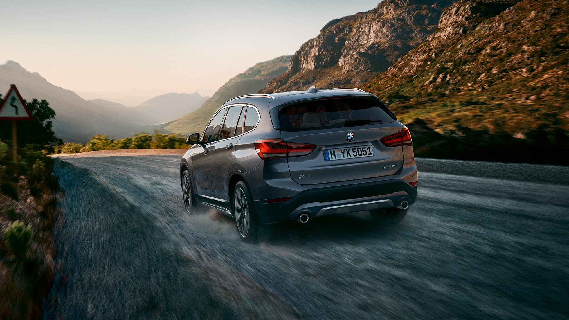 BMW X1, tročetvrinski stražnji prikaz. BMW X1, tročetvrinski stražnji prikaz vožnje kroz planine.