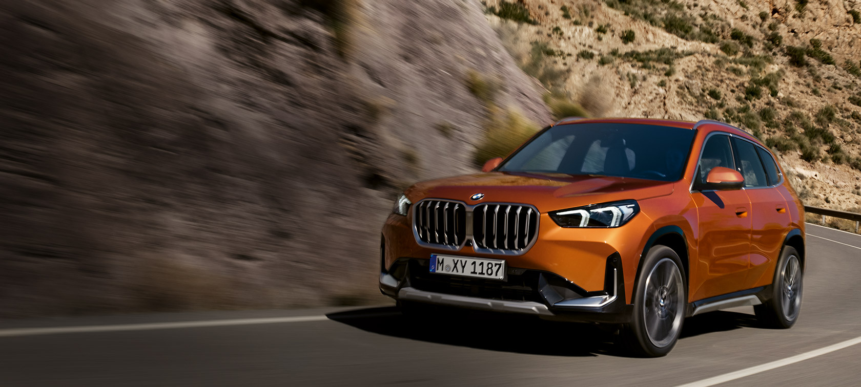 BMW X1 U11 xLine Utah orange metalik tročetvrtinski pogled sprijeda u vožnji na seoskoj cesti