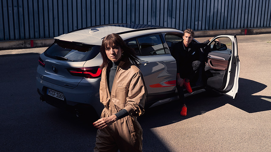 BMW X2 F39 Brooklyn Grey tročetvrtinski pogled straga sa otvorenim vratima i dvije osobe BMW X2 F39 Brooklyn Grey tročetvrtinski pogled straga sa otvorenim vratima i dvije osobe