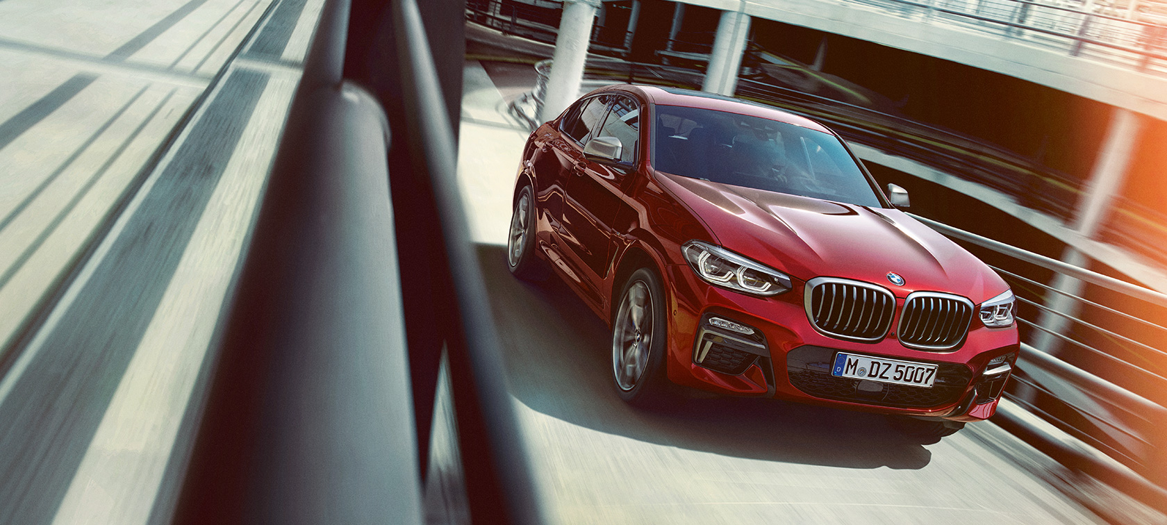 BMW X4 u vožnji parkingom BMW X4 G02 2018 Flamenco Red s briljantnim efektom tročetvrtinski bočni pogled na parkiralištu