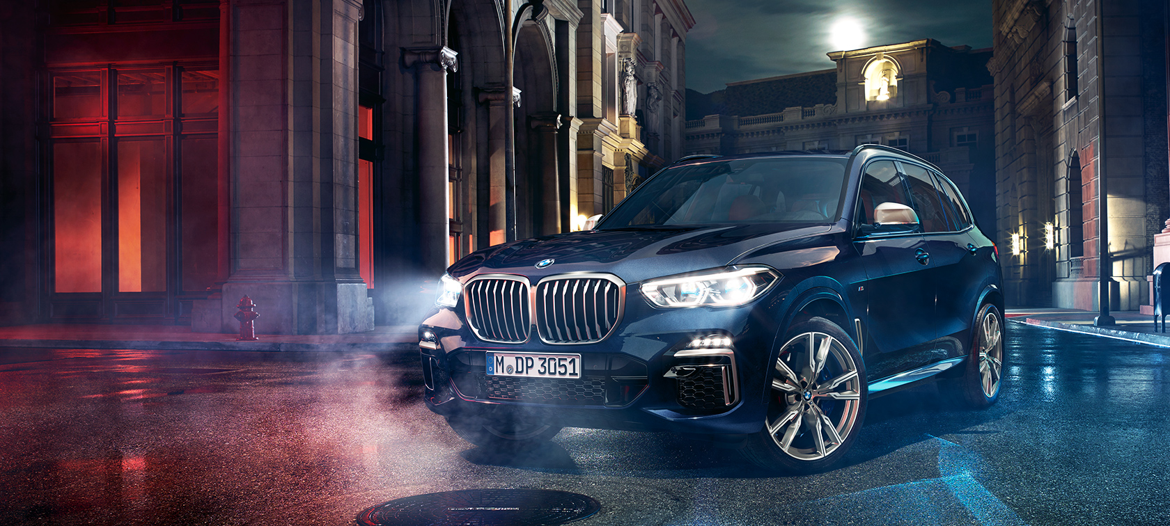 BMW X5 M50d na cesti BMW X5 M50d stoji na cesti noću s gradom u pozadini