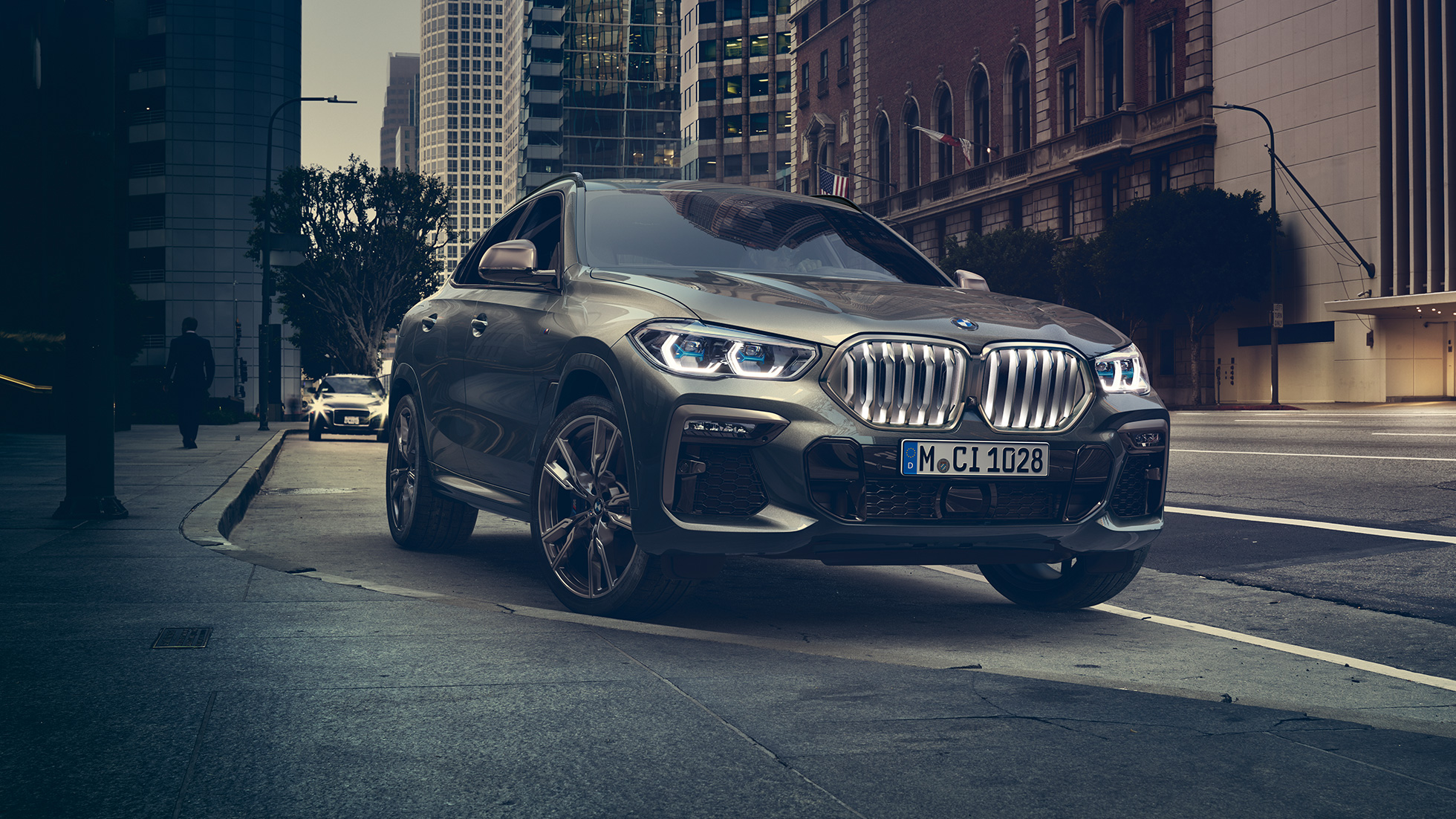 BMW X6 prilagodljiv M ovjes Professional BMW X6 u tročetvrtinskom prikazu prednjeg kraja ispred urbanog okruženja.