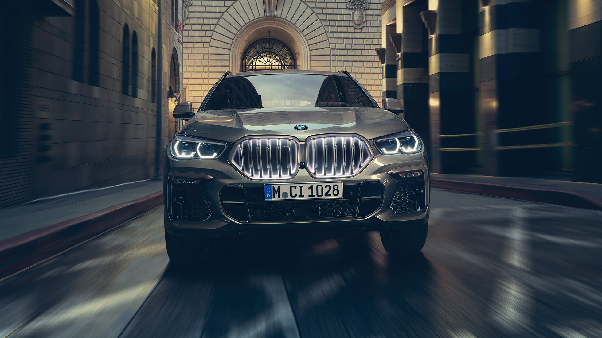 BMW X6 s BMW ‘Iconic Glow’ rešetkom maske. Prikaz prednjeg kraja BMW-a X6 ispred urbanog okruženja.