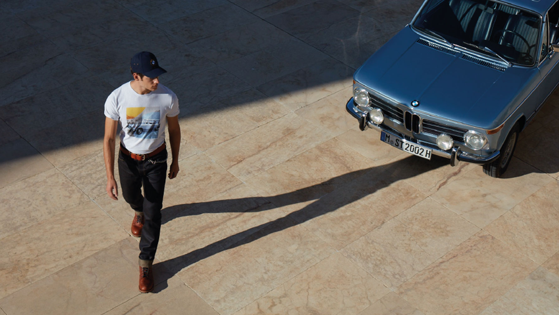 Muškarac nosi BMW Classic mušku majicu i divi se klasičnom BMW-u. Muškarac nosi BMW Classic mušku majicu i divi se klasičnom BMW-u.