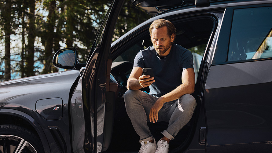 Muškarac sjedi u BMW-u i gleda u pametni telefon BMW Proljeće Ljeto dodaci Muškarac sjedi u BMW-u i gleda u pametni telefon