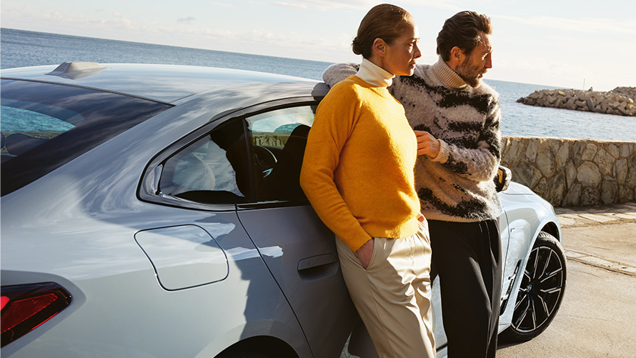 Trajanje BMW Service Inclusive paketa i ugovorna razdoblja za nove automobile BMW Service Inclusive muškarac i žena naslonjeni na BMW i4 ispred obale