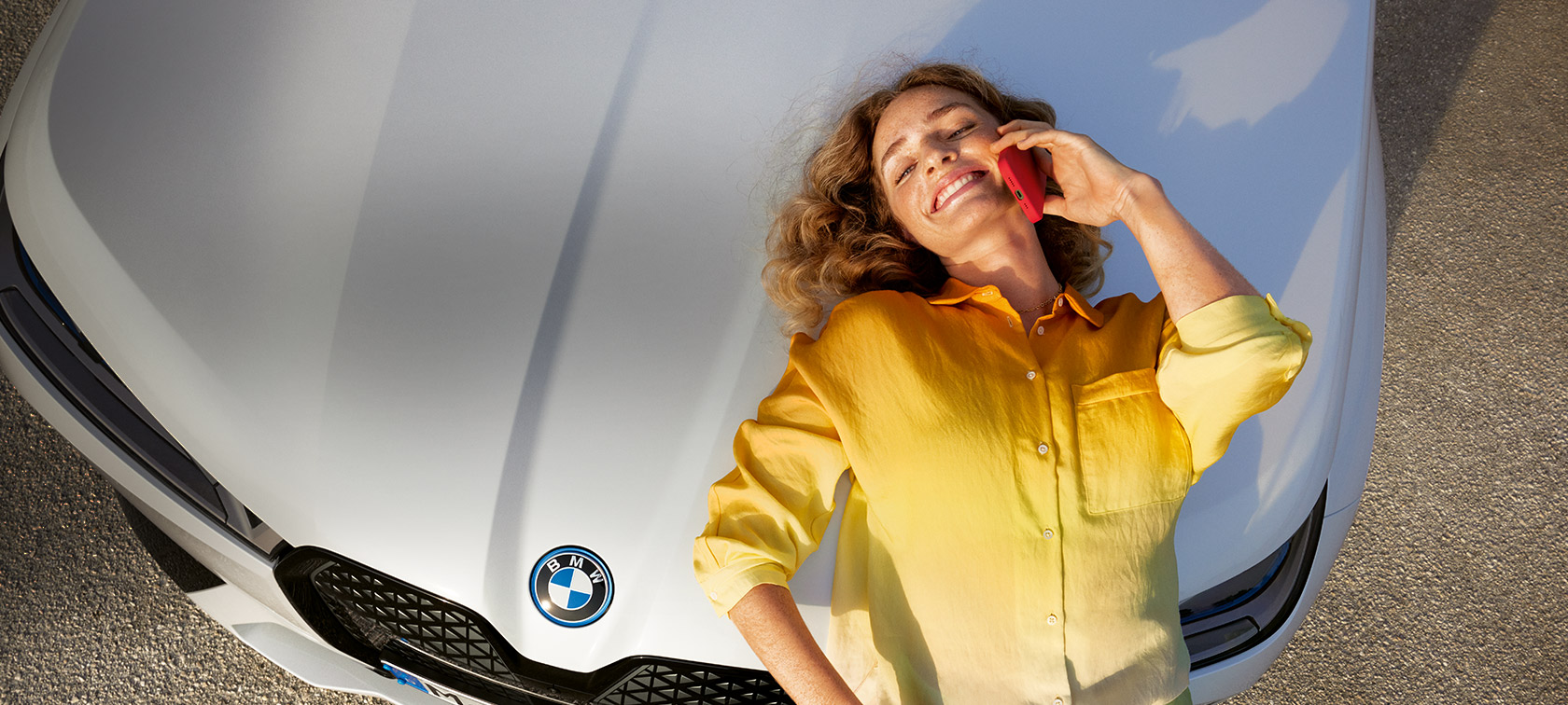 Opustite se, brinemo se za proactive care, preglede i održavanje Proaktivna njega, pregled i održavanje Relax We Care Žena sa žutom košuljom i pametnim telefonom u ruci naslonjena na bijeli BMW poklopac motora